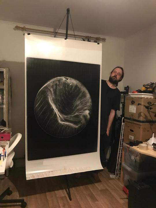 A man with a beard stands next to a large print of a circular abstract image.