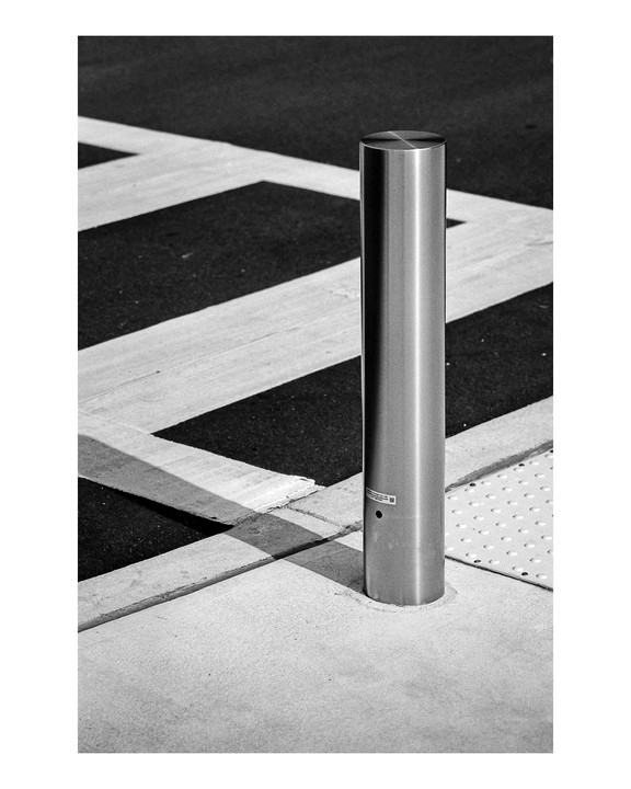 A metal bollard stands on a sidewalk next to a street with painted lines.