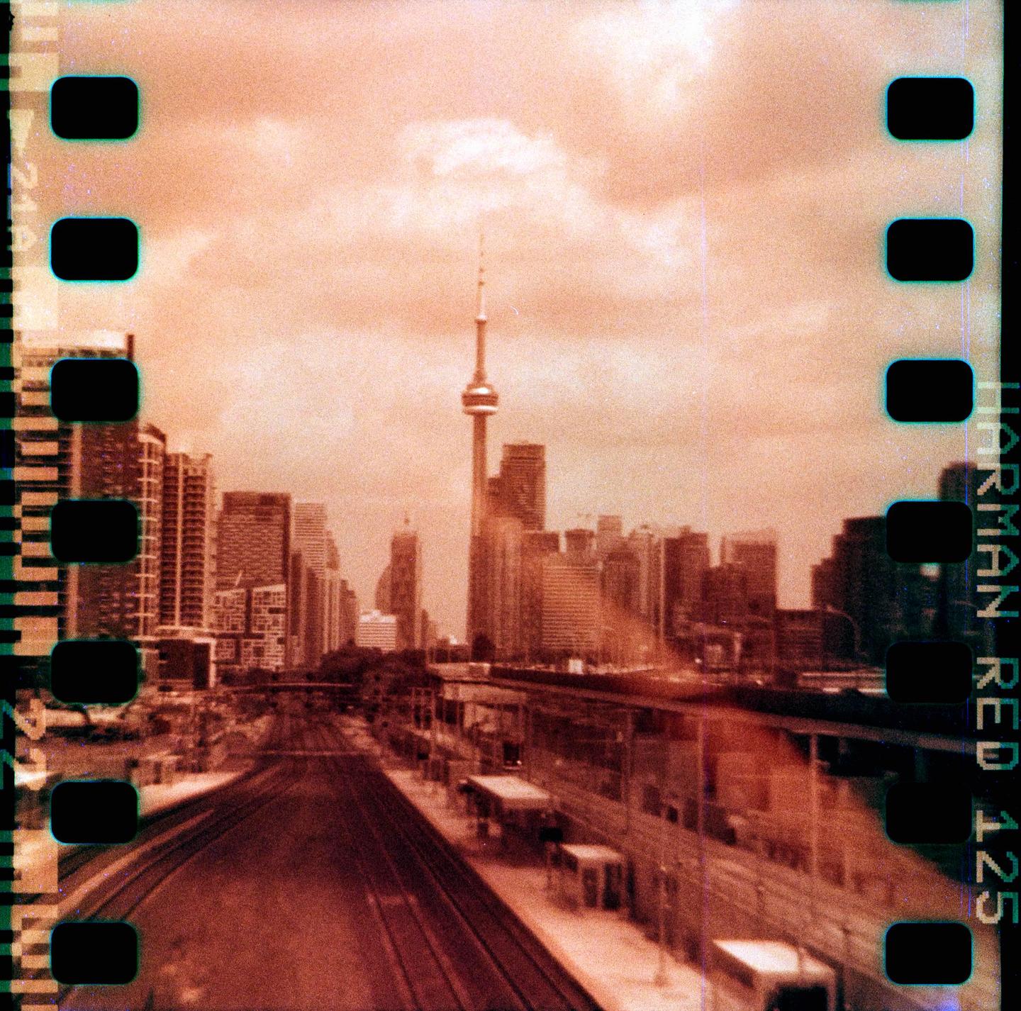 A cityscape with a prominent tower and numerous buildings is seen from above a train track and station.