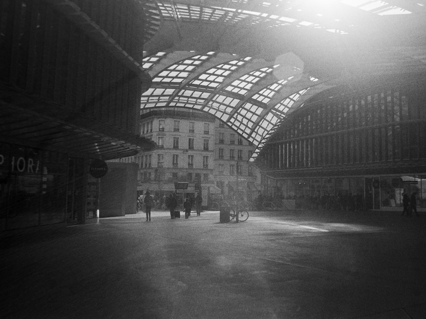 A street with people and a bicycle is visible under a large arched roof, with a building in the background.