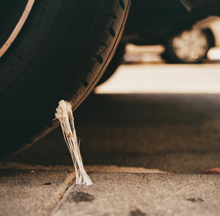 A piece of white chewing gum is stuck between a car tire and the concrete ground.