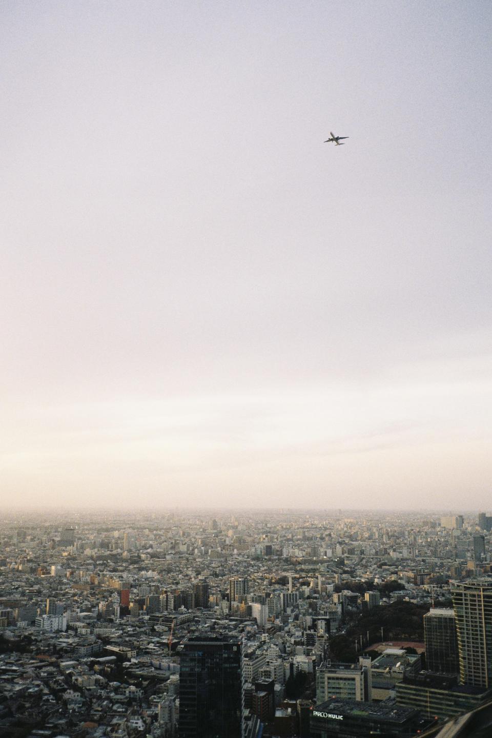 An airplane flies high above a sprawling city with numerous buildings under a hazy sky.