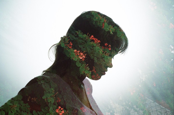 A double exposure shows a woman's profile overlaid with green foliage and red flowers.