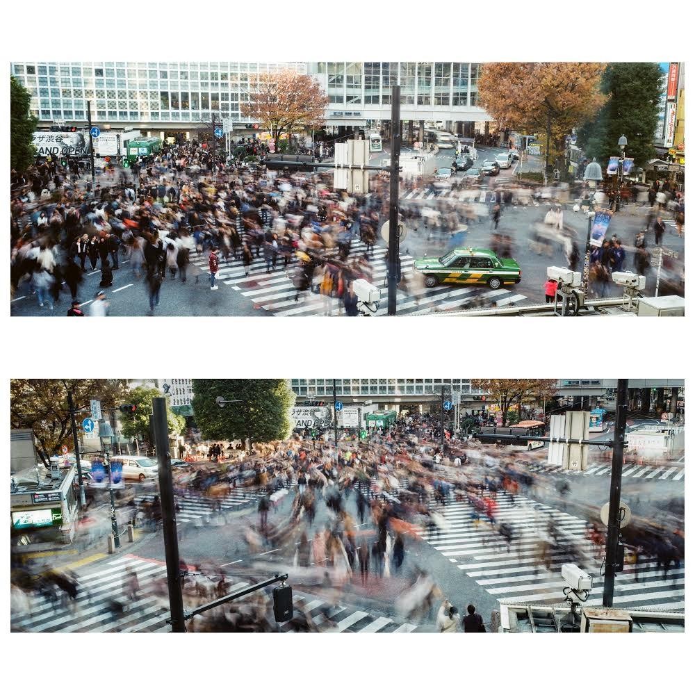 A long exposure captures the movement of a crowd crossing a street in a city.