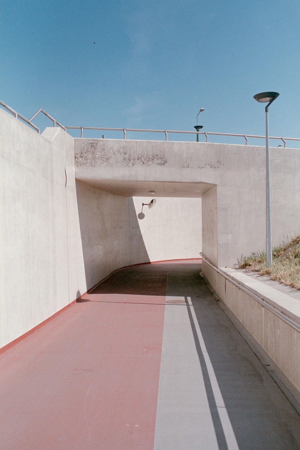 A pedestrian underpass with a red path and strong shadows is visible under a clear blue sky.