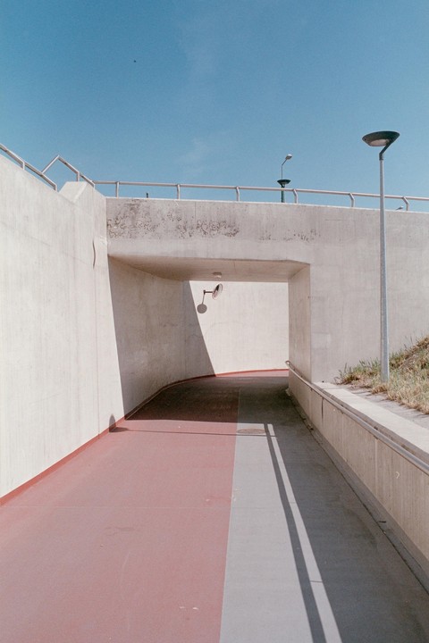 A pedestrian underpass with a red path and strong shadows is visible under a clear blue sky.