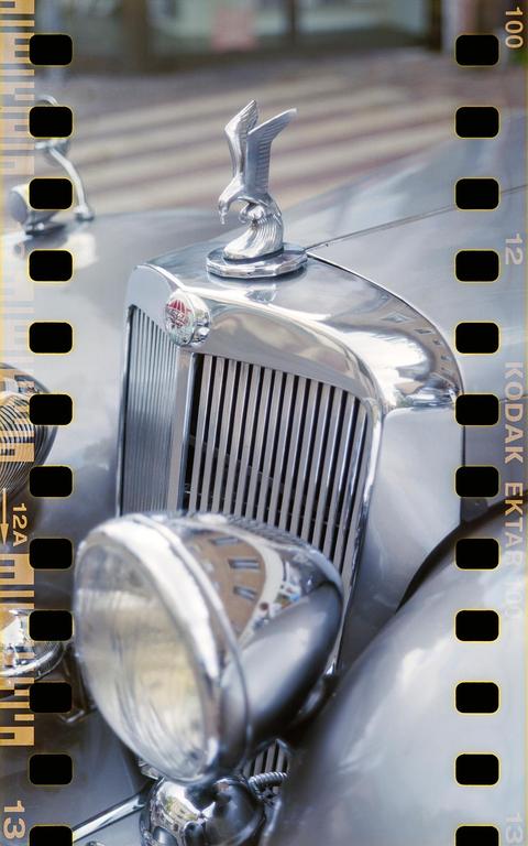 A chrome eagle hood ornament sits on the front of a vintage car with a large headlight and grille.