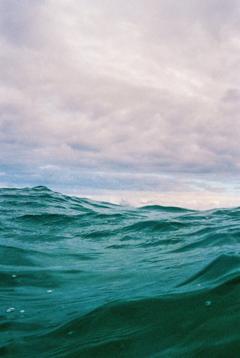 The ocean surface shows waves under a cloudy sky.