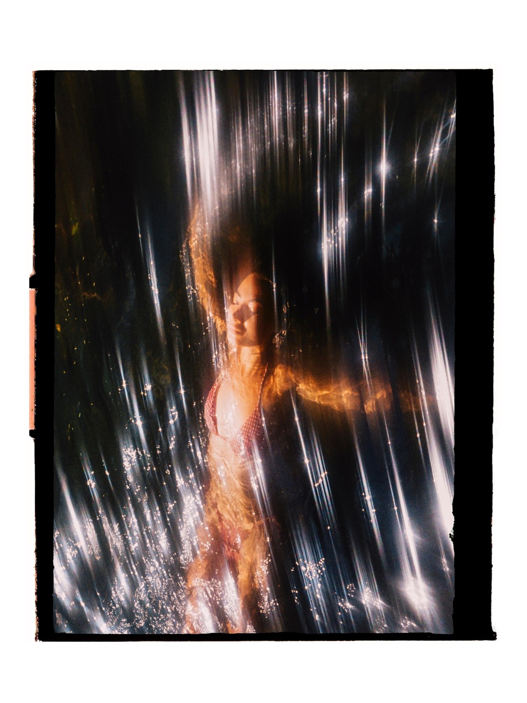 A woman with long hair is submerged in water with light reflecting off the surface.