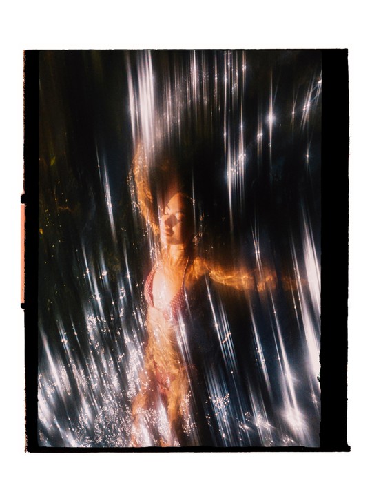 A woman with long hair is submerged in water with light reflecting off the surface.