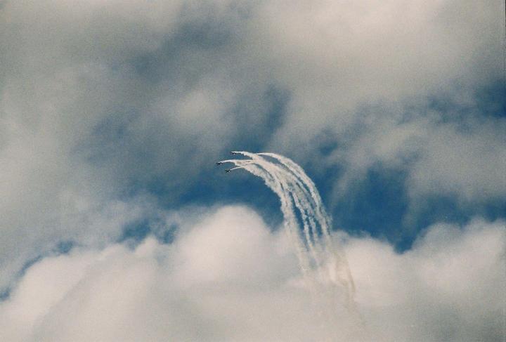 Three airplanes fly in formation, leaving white trails against a blue sky with clouds.