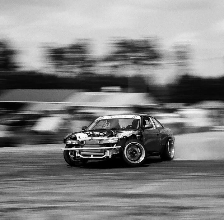 A car with its front bumper removed drifts on a track, creating a motion blur effect.