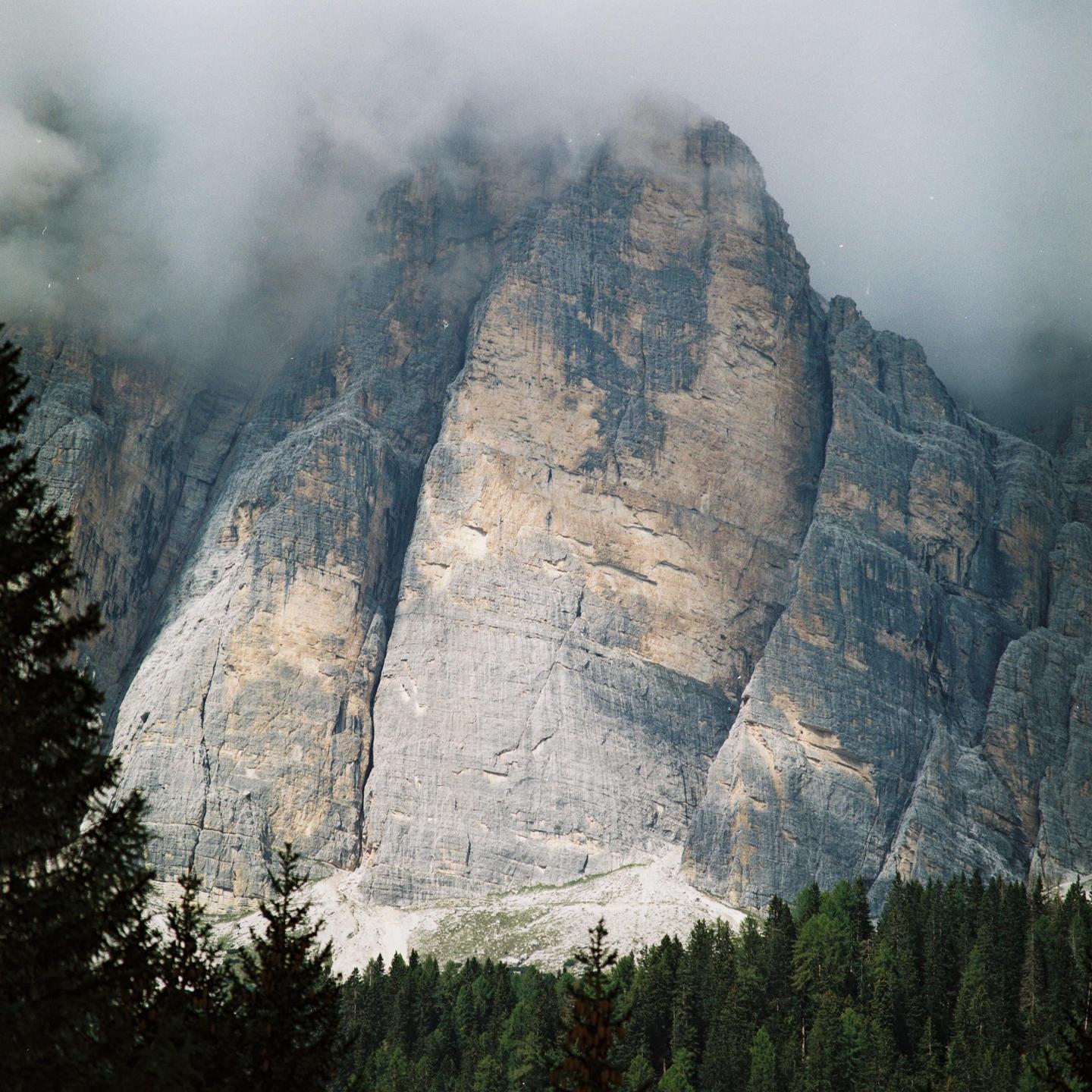 A large, rocky mountain is partially obscured by clouds, with a dense forest at its base.