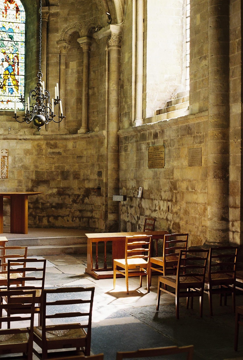 Sunlight streams through a tall window, illuminating a wooden chair in a stone church interior.