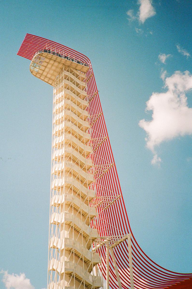 A tall observation tower with a red and white striped canopy stands against a bright blue sky with a few clouds.
