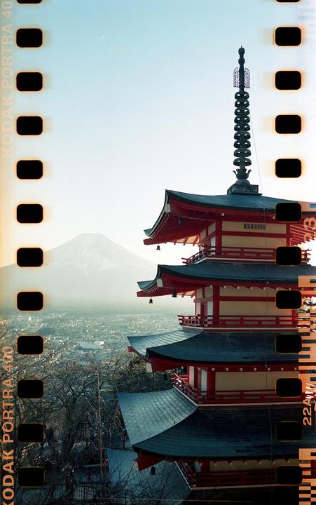 A red and black pagoda stands on a hill overlooking a city with a snow-capped mountain in the background.