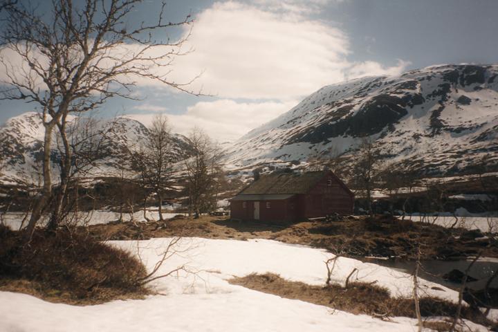 A red house sits in a snowy valley with mountains in the background.