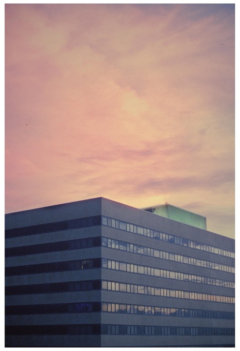 A building with many windows is visible under a pink and orange sky.
