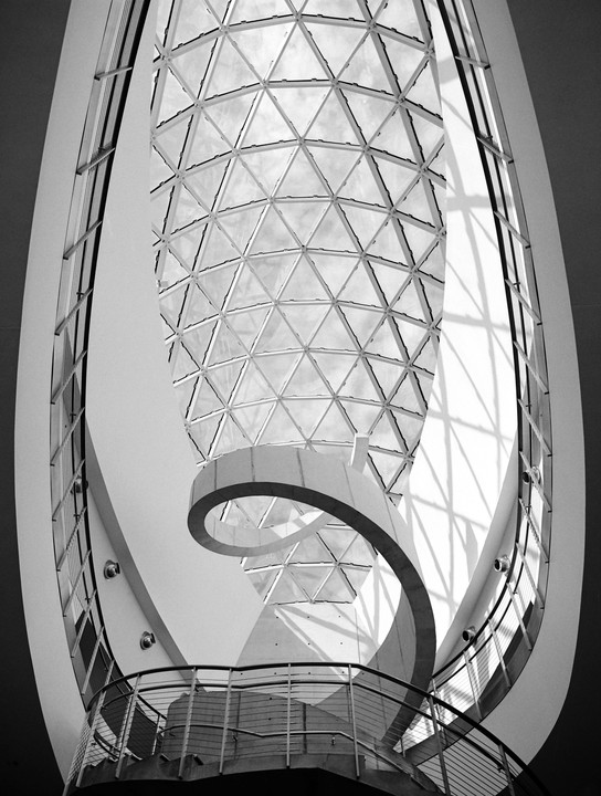 A spiral staircase curves beneath a triangular glass ceiling in a modern building.