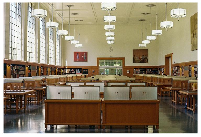 A large library reading room with tall windows, long wooden tables, and hanging circular lights.