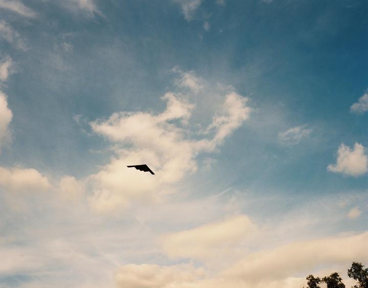 A stealth bomber flies across a partly cloudy sky.