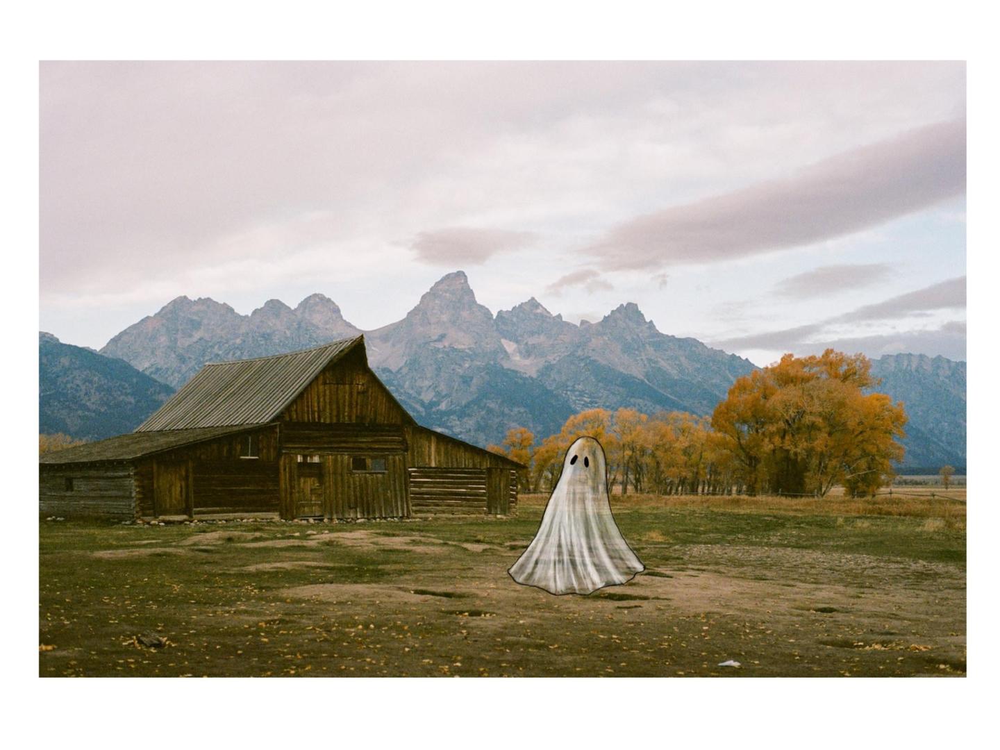 A ghost stands in a field in front of a wooden barn with mountains and autumn trees in the background.