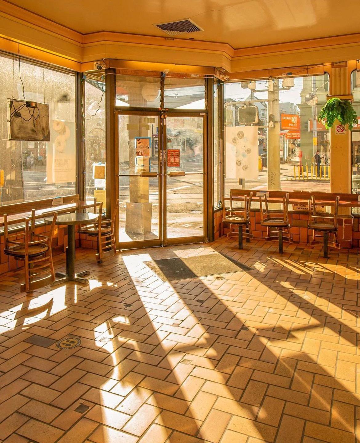 Sunlight streams through the windows of an empty donut shop, casting long shadows across the tiled floor.