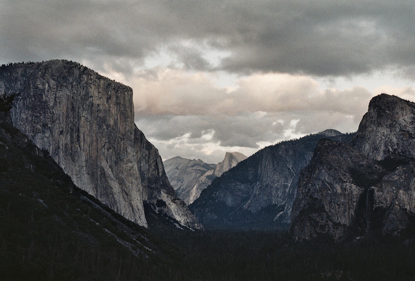 A valley with steep rock faces on either side is visible under a cloudy sky.