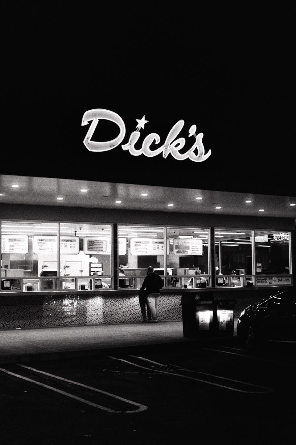 A man stands at a brightly lit Dick's restaurant counter at night.
