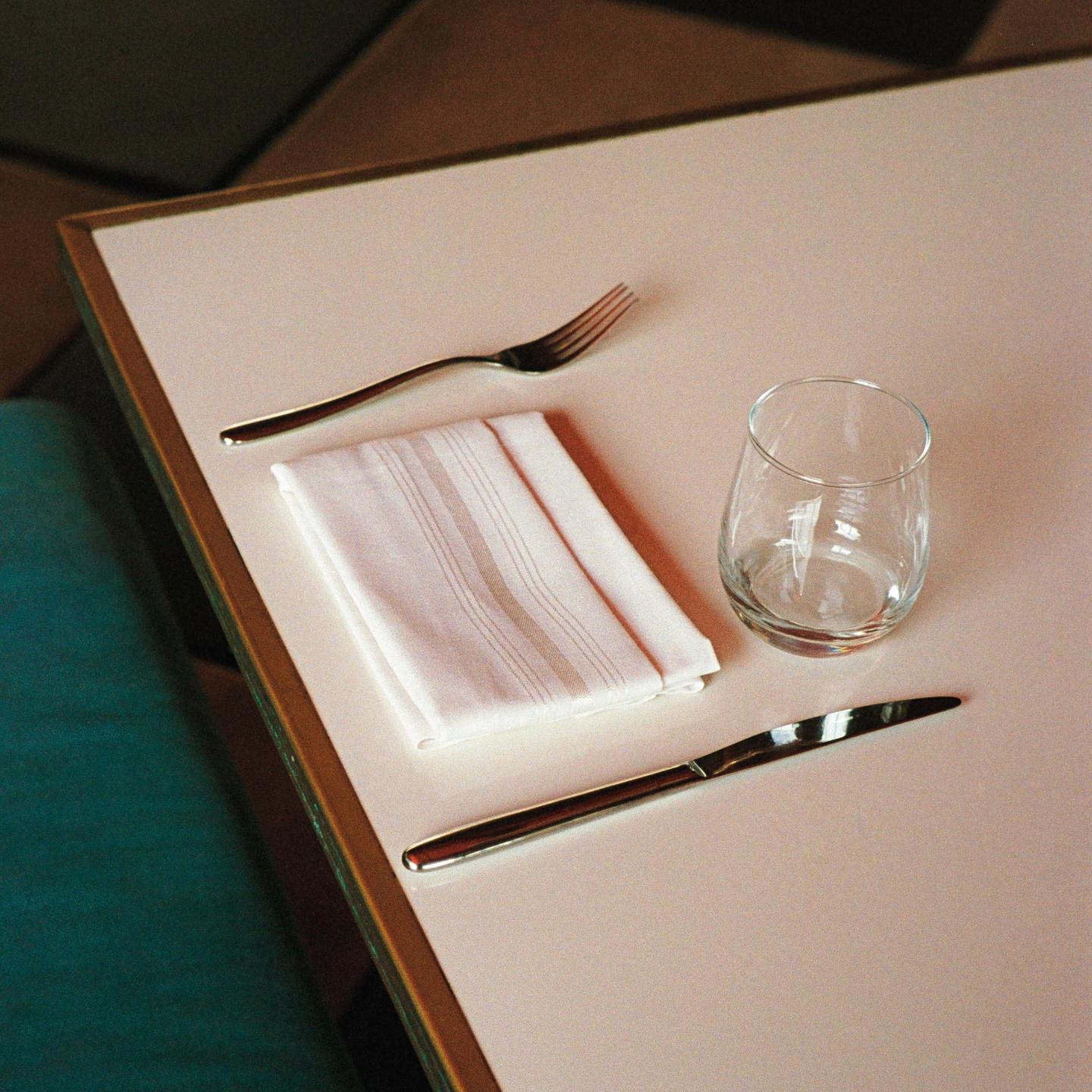 A fork, napkin, glass, and knife are arranged on a table.