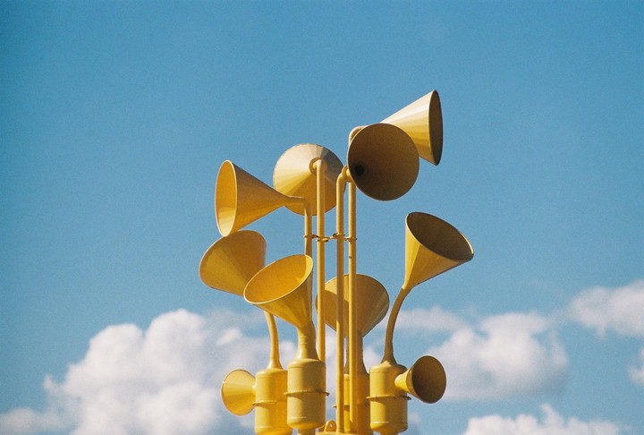 A yellow sculpture with multiple horn-like shapes stands against a bright blue sky with white clouds.