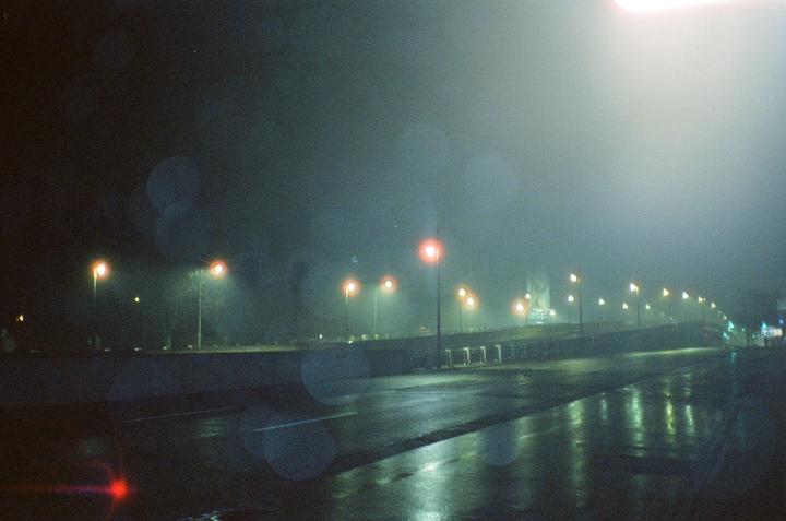 A foggy night scene shows a wet road reflecting the light from numerous streetlights.