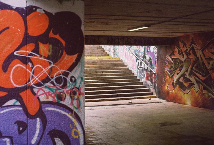 A graffiti-covered underpass leads to a set of stairs with a metal handrail.