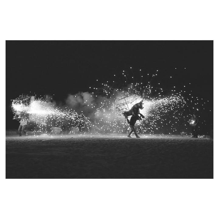 Two men in costume walk across a dark field at night, surrounded by fireworks.