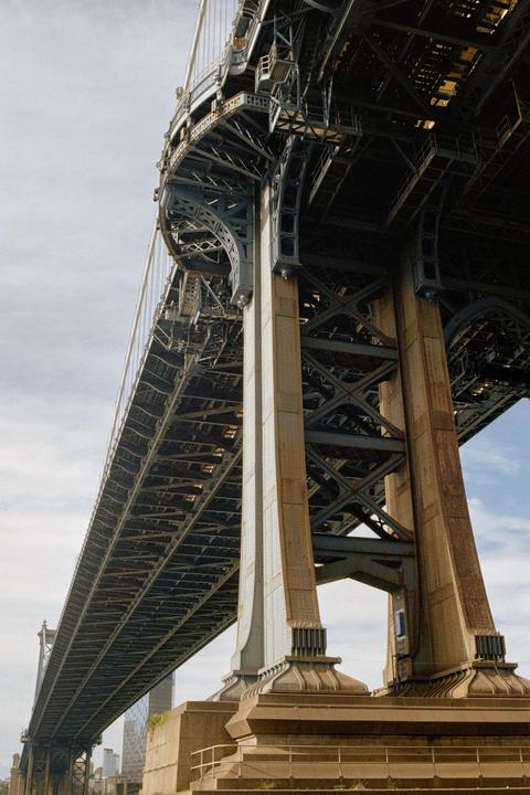 A low-angle view shows the underside of a large metal bridge with intricate support structures.