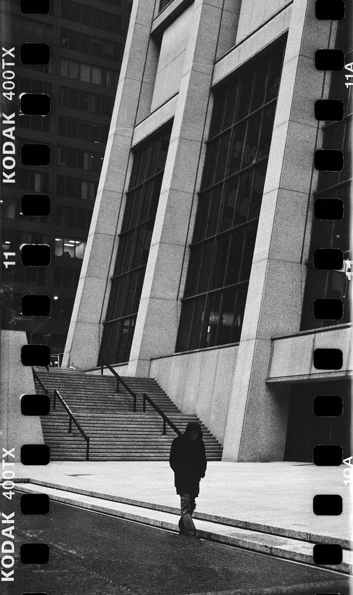 A person walks away from the camera on a paved path next to a large building with stairs.