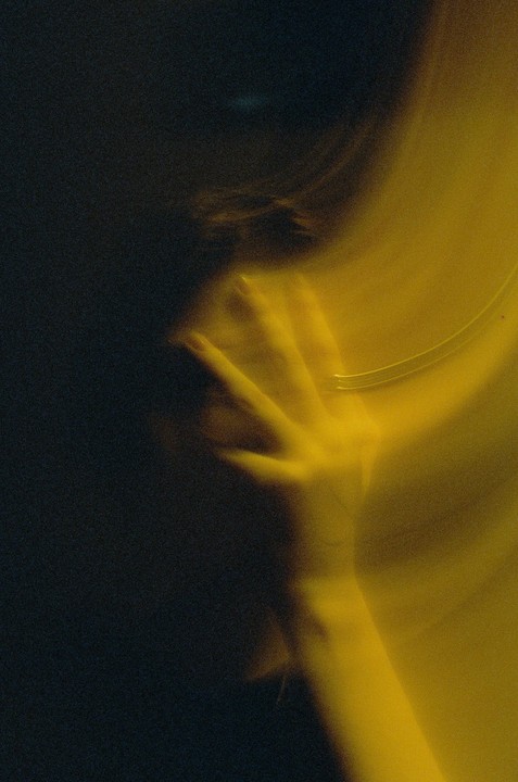 A hand with a ring is visible in a dark, blurry image with a yellow light source.