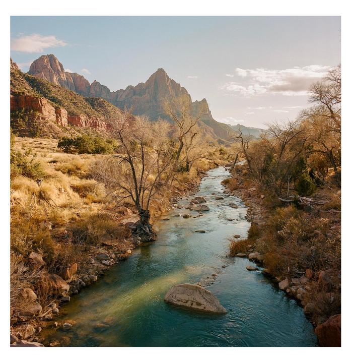 A river flows through a valley with mountains in the background under a partly cloudy sky.