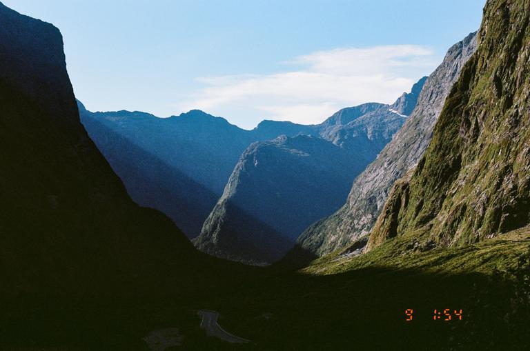 Sunlight illuminates a valley between two mountains, with a road visible at the bottom.