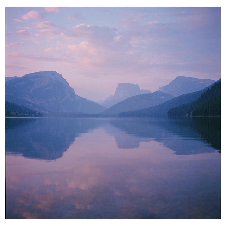A lake reflects the purple and pink sky and mountains at sunrise.