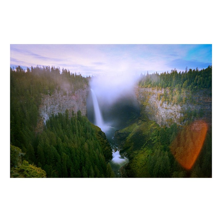 A waterfall cascades into a canyon filled with trees and mist under a cloudy sky.