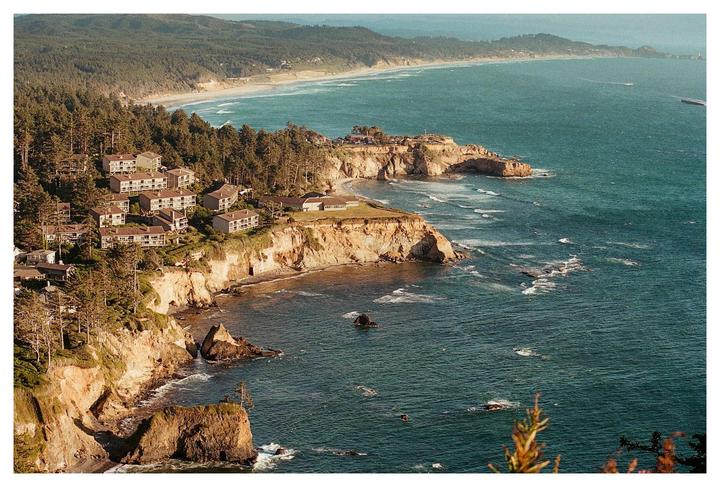 A coastal town with houses nestled among trees on cliffs overlooking the ocean.