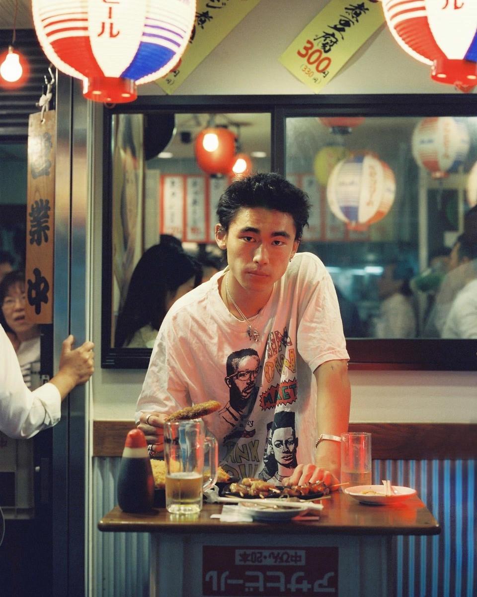 A man sits at a table with food and a drink in a restaurant at night.