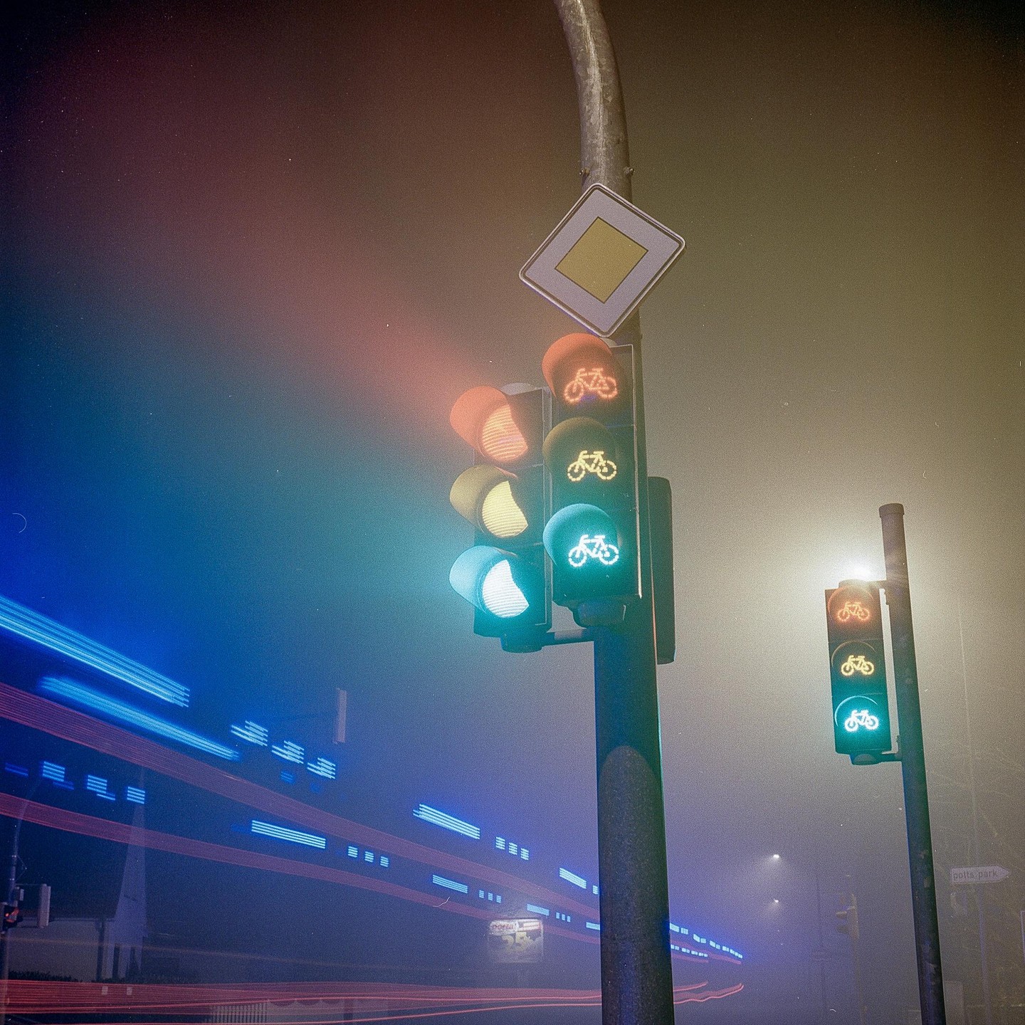 A traffic light with bicycle symbols glows in the fog at night, with light trails from passing vehicles.