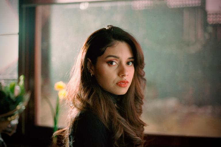 A woman with long wavy hair and a nose ring looks directly at the viewer.
