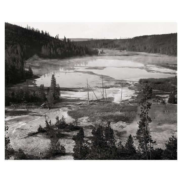 A body of water with steam rising from it is surrounded by a forest.