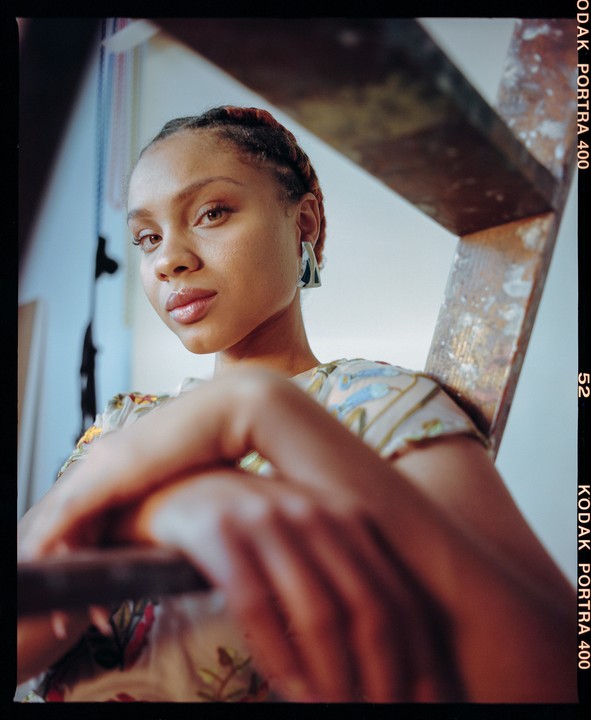 A woman with braided hair and a patterned shirt is looking at the viewer.