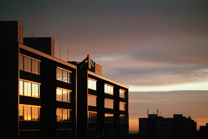 The windows of a dark building reflect the golden light of a sunset sky.
