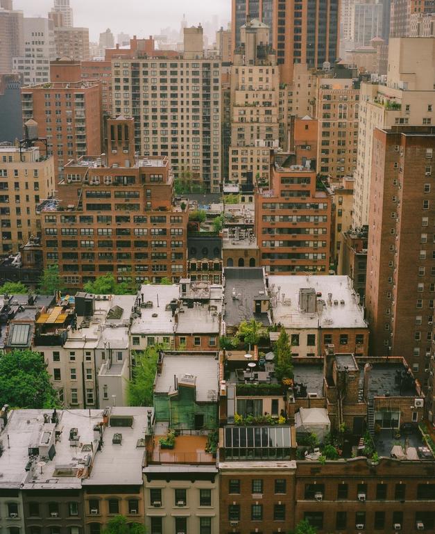 An aerial view shows a dense urban landscape of buildings and rooftops under a gloomy sky.