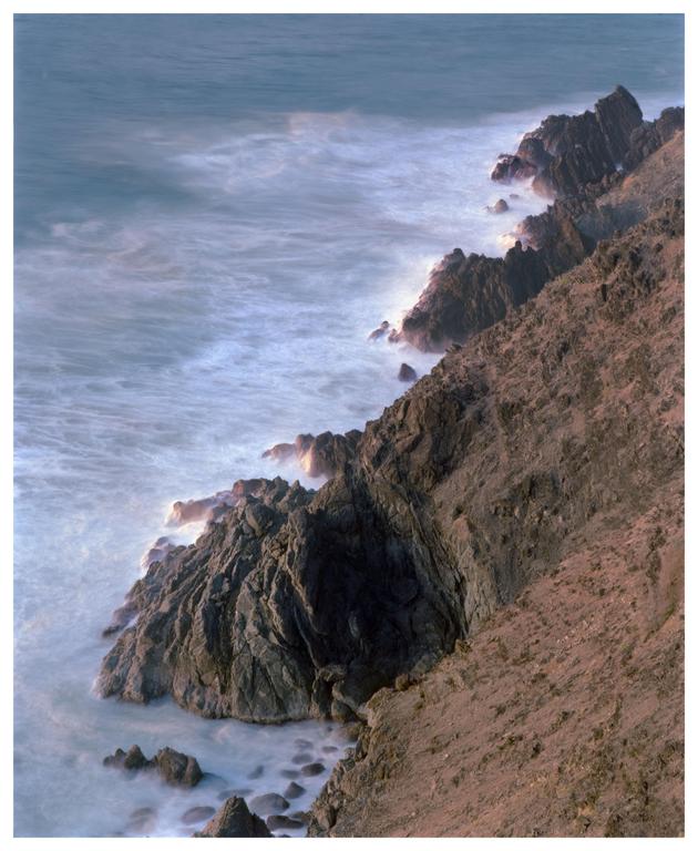 Waves crash against a rocky coastline under a soft, diffused light.